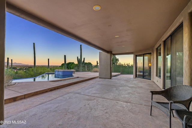 patio terrace at dusk featuring a swimming pool with hot tub