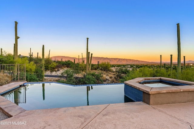 pool at dusk featuring a mountain view and an in ground hot tub