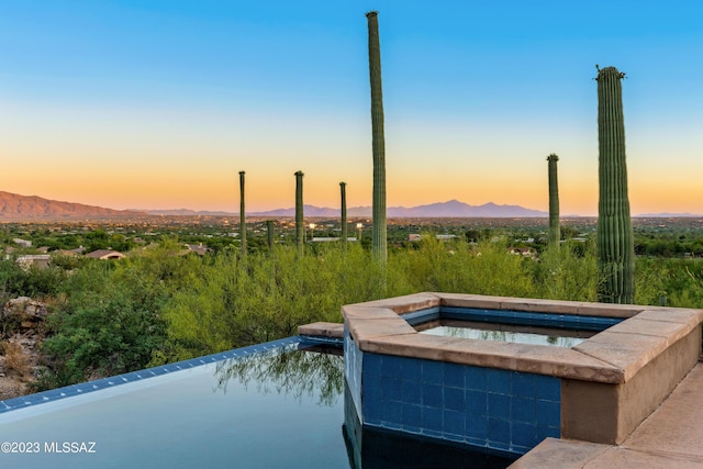 pool at dusk featuring a mountain view and an in ground hot tub