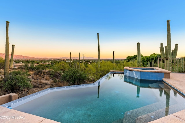 pool at dusk with an in ground hot tub