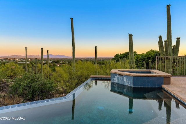 pool at dusk featuring an in ground hot tub and a mountain view