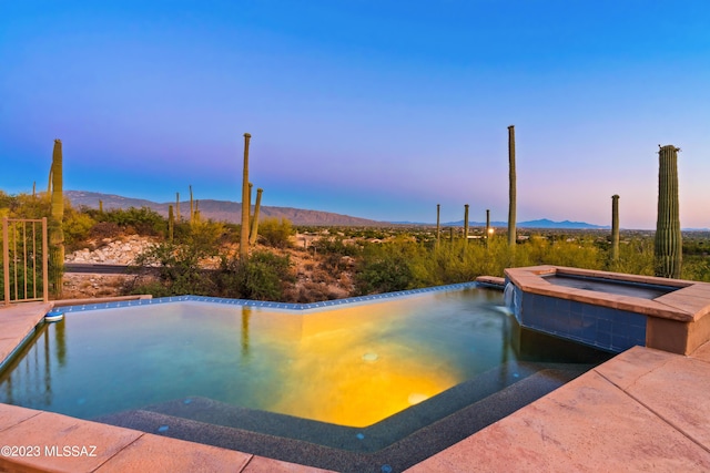 pool at dusk featuring a mountain view and an in ground hot tub