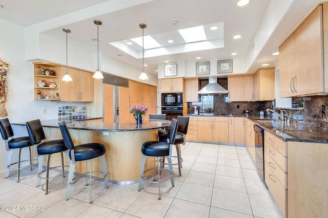 kitchen with light brown cabinets, pendant lighting, dark stone counters, wall chimney range hood, and black appliances