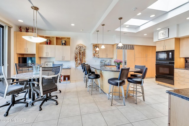 kitchen with black appliances, hanging light fixtures, light brown cabinetry, and light tile patterned floors