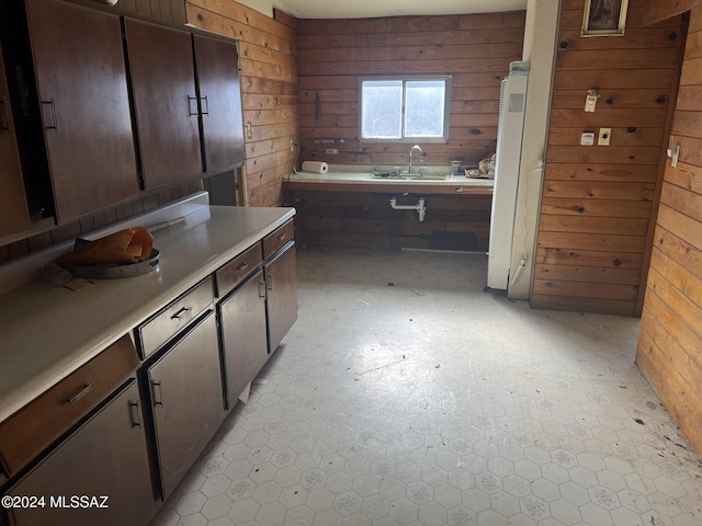 kitchen with sink, dark brown cabinetry, and wood walls