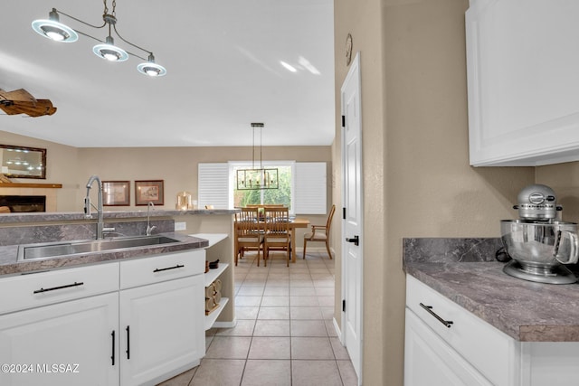 kitchen featuring a tile fireplace, pendant lighting, white cabinetry, and sink