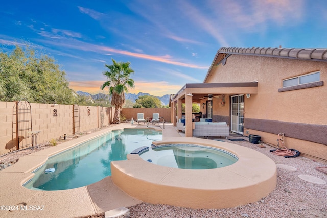 pool at dusk with an in ground hot tub, a patio, an outdoor hangout area, and ceiling fan