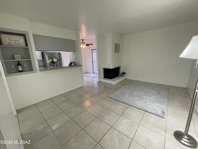 unfurnished living room featuring tile patterned flooring, a large fireplace, and ceiling fan