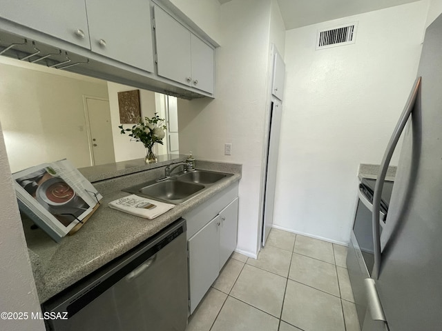 kitchen featuring visible vents, a sink, stainless steel dishwasher, freestanding refrigerator, and light tile patterned flooring