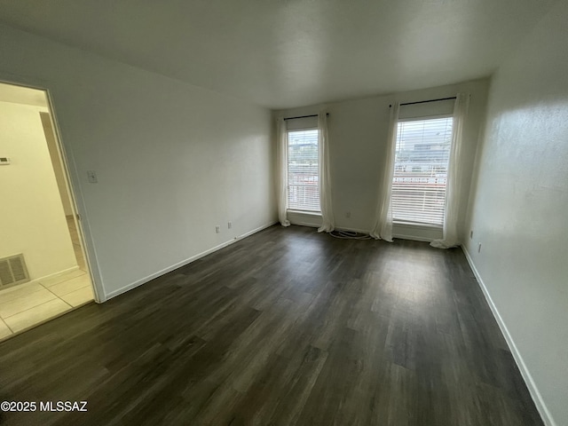 empty room with visible vents, dark wood-type flooring, and baseboards