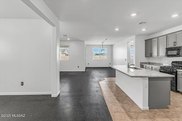 kitchen featuring light stone countertops, gray cabinetry, sink, black appliances, and an island with sink