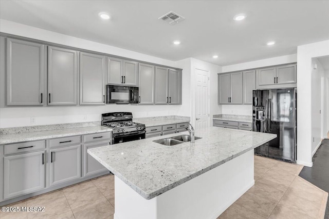 kitchen featuring light stone countertops, gray cabinetry, sink, black appliances, and an island with sink