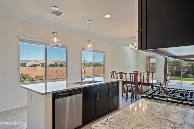 kitchen featuring stainless steel dishwasher, light stone countertops, sink, and an island with sink