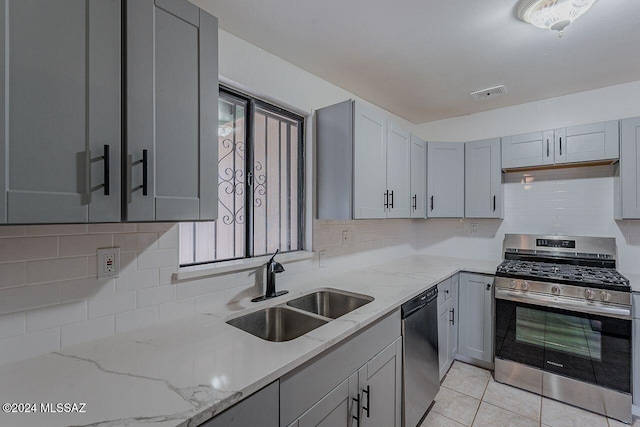 kitchen with gray cabinetry, light stone countertops, sink, light tile patterned floors, and appliances with stainless steel finishes