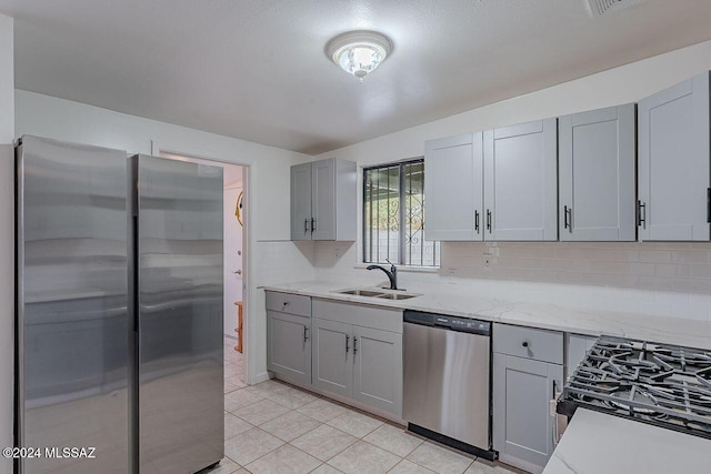 kitchen with gray cabinetry, sink, light stone counters, decorative backsplash, and appliances with stainless steel finishes