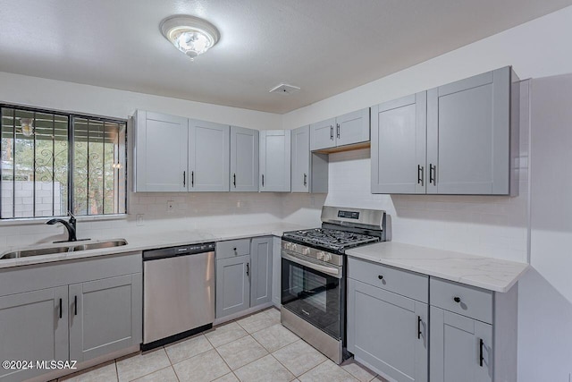 kitchen with gray cabinetry, light stone countertops, sink, light tile patterned floors, and appliances with stainless steel finishes