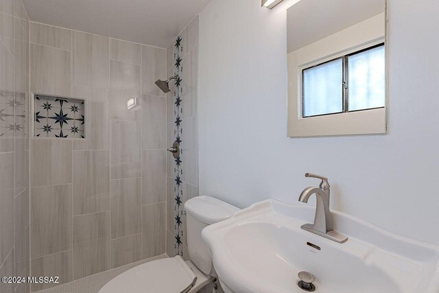 bathroom with tiled shower, toilet, and sink