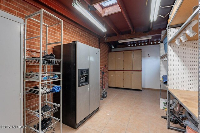 basement featuring a workshop area, stainless steel fridge, light tile patterned floors, and brick wall