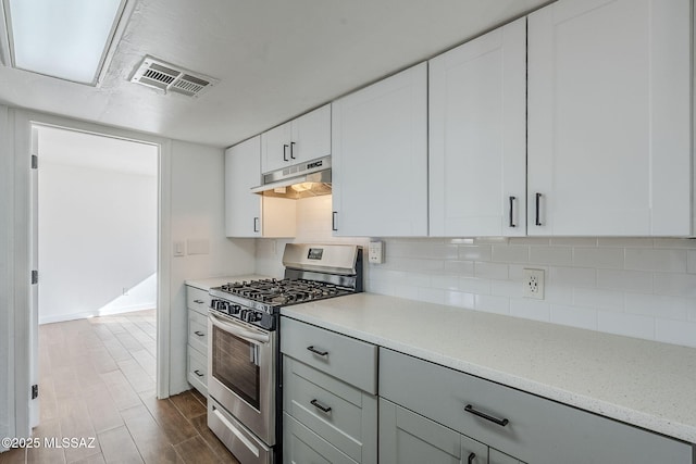 kitchen with dark wood-type flooring, white cabinetry, tasteful backsplash, light stone countertops, and gas stove