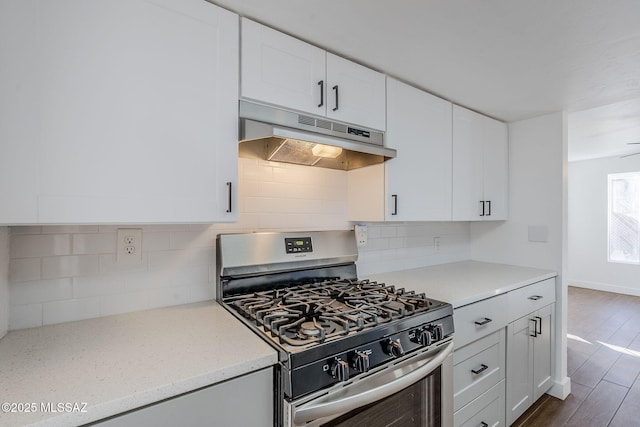 kitchen with white cabinets, backsplash, light stone counters, gas stove, and dark wood-type flooring