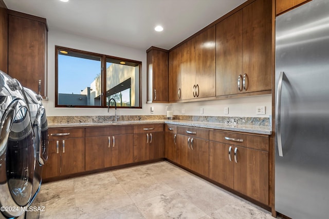 kitchen with stainless steel refrigerator, light stone countertops, and sink