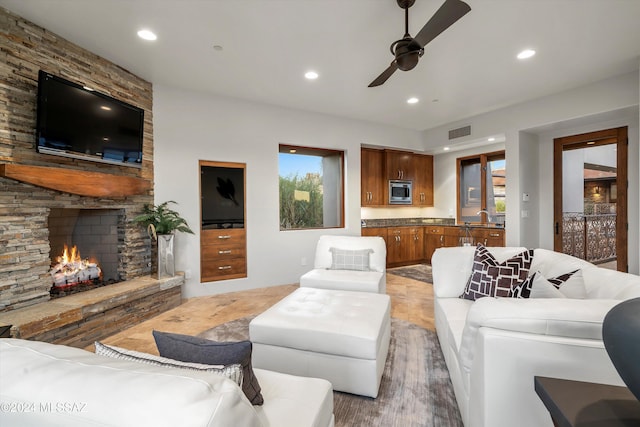 living room featuring hardwood / wood-style floors, ceiling fan, a stone fireplace, and sink