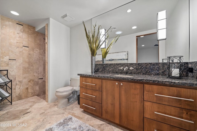 bathroom with a tile shower, vanity, and toilet