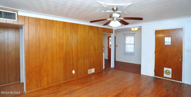 unfurnished room with ceiling fan, wood walls, crown molding, and dark hardwood / wood-style floors