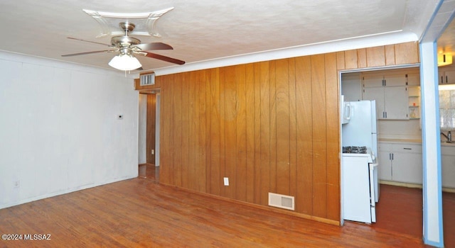 empty room with wood-type flooring, ceiling fan, ornamental molding, and wood walls