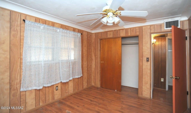 unfurnished bedroom featuring ceiling fan, a closet, dark wood-type flooring, and wood walls