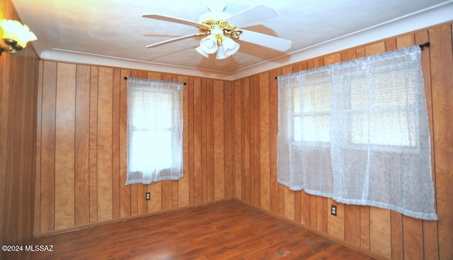 unfurnished room with wooden walls, ceiling fan, and dark wood-type flooring