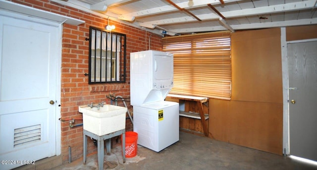 washroom featuring sink, stacked washer and dryer, and brick wall