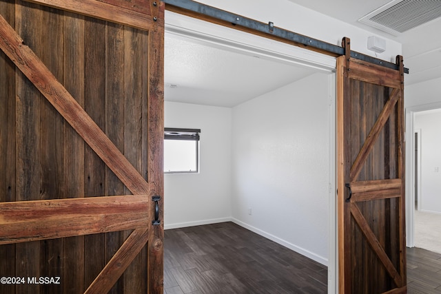 interior space featuring a barn door, dark wood-style flooring, visible vents, and baseboards