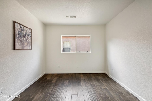 empty room featuring baseboards, visible vents, and dark wood finished floors