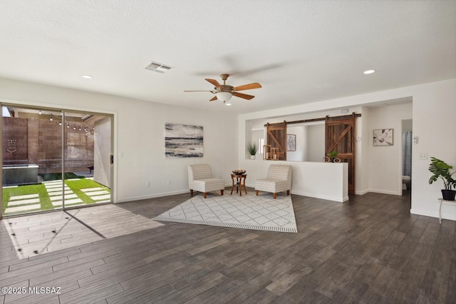 sitting room featuring ceiling fan, a barn door, wood finished floors, visible vents, and baseboards