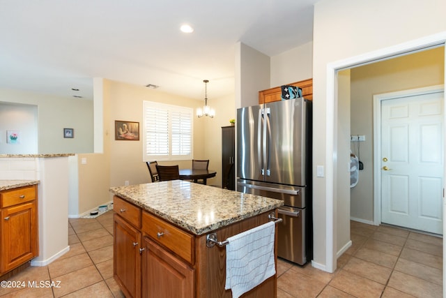 kitchen with stainless steel refrigerator, light stone countertops, a kitchen island, and pendant lighting