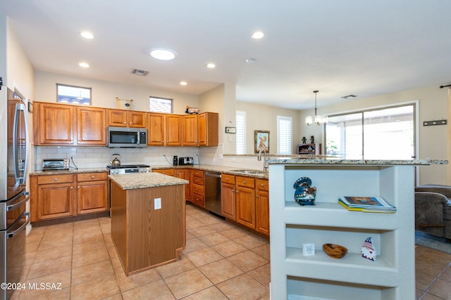 kitchen with kitchen peninsula, appliances with stainless steel finishes, sink, a kitchen island, and hanging light fixtures