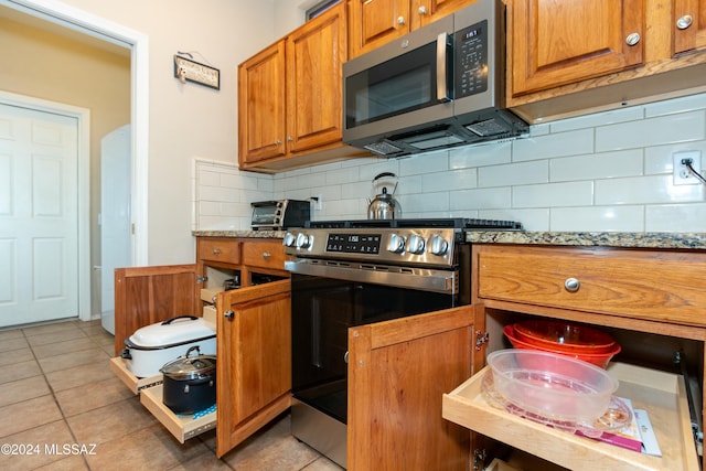 kitchen with decorative backsplash, light tile patterned flooring, light stone counters, and appliances with stainless steel finishes