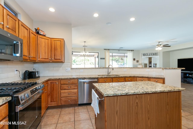 kitchen with sink, a center island, light stone counters, ceiling fan with notable chandelier, and appliances with stainless steel finishes