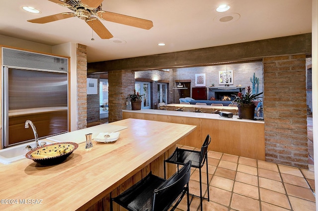 kitchen with a breakfast bar, ceiling fan, sink, light tile patterned floors, and built in refrigerator