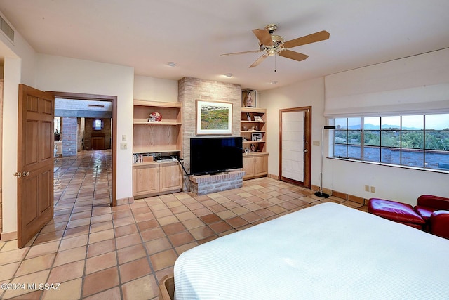 bedroom featuring ceiling fan, a large fireplace, and light tile patterned floors