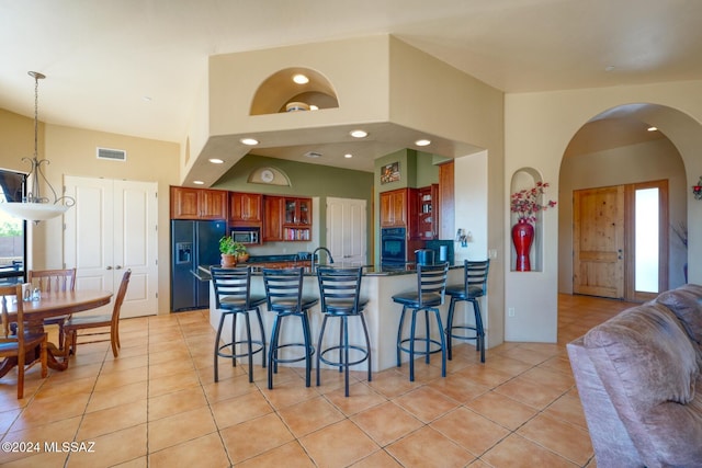 kitchen featuring black appliances, light tile patterned floors, a towering ceiling, a kitchen bar, and kitchen peninsula