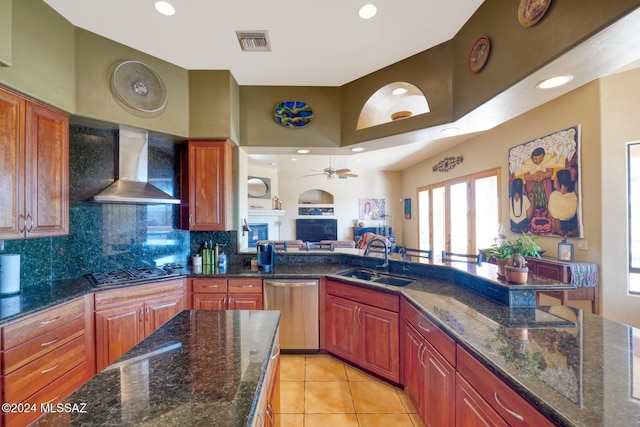 kitchen with sink, stainless steel appliances, wall chimney range hood, dark stone counters, and light tile patterned floors