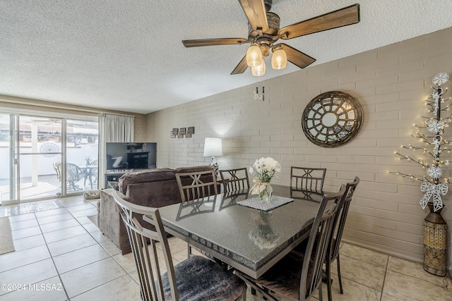 tiled dining room featuring ceiling fan, brick wall, and a textured ceiling