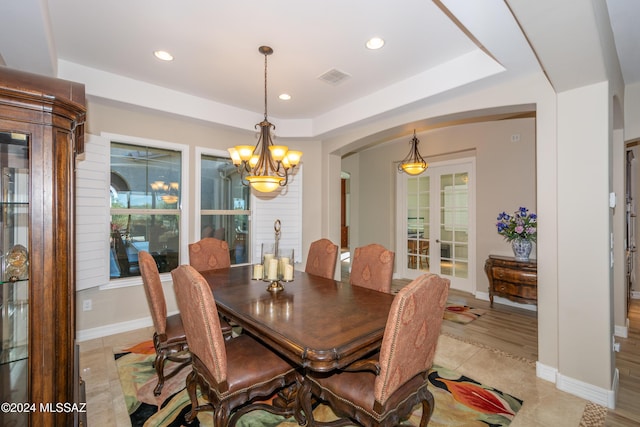 dining area with a tray ceiling, light tile patterned flooring, and a chandelier