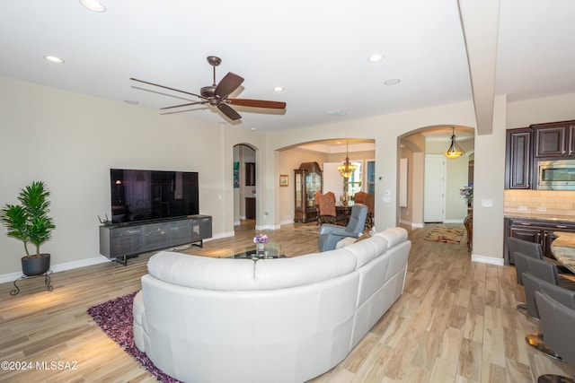 living room featuring ceiling fan with notable chandelier and light hardwood / wood-style flooring