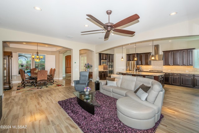 living room featuring ceiling fan with notable chandelier and light hardwood / wood-style flooring