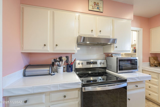 kitchen with white cabinets, stainless steel appliances, tile counters, and range hood