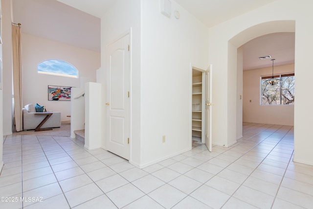 hallway with light tile patterned floors, visible vents, stairway, and arched walkways