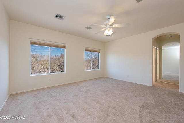 empty room featuring light carpet, ceiling fan, visible vents, and arched walkways